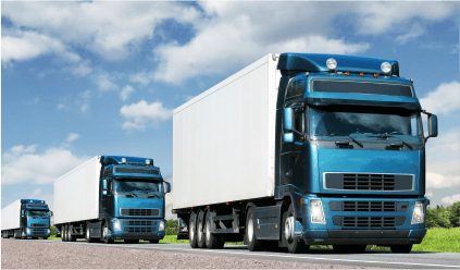 A trio of semi trucks driving side by side on a road, surrounded by green fields.